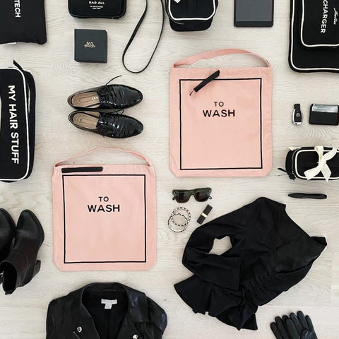 Bag-all To Wash Laundry Bag in pink cotton with black text, shown in flatlay with black accessories and shoes on white background, featuring drawstring closure and hanging handle for closet organization