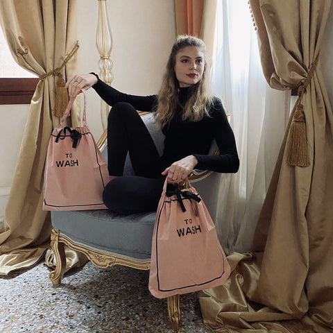 Bag-all pink To Wash Laundry Bag displayed on vintage chair, featuring drawstring closure and black text design, perfect for stylish laundry organization