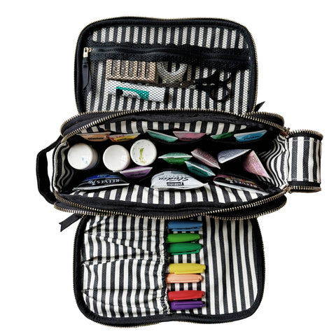 Open striped cream travel organizer with compartments holding markers, bottles, scissors, and small craft supplies inside