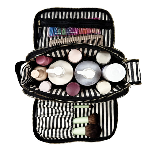 Top view of a black and white striped beauty organizer with bottles, brushes, and nail polish inside compartments and mesh pockets.