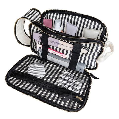 Cream triple compartment beauty and toiletry organizer with mesh pockets and elastic loops holding various grooming items.