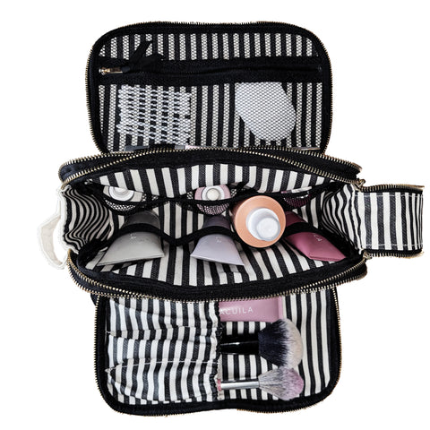 Open black and white striped toiletry organizer with beauty products and brushes inside compartments and mesh pockets