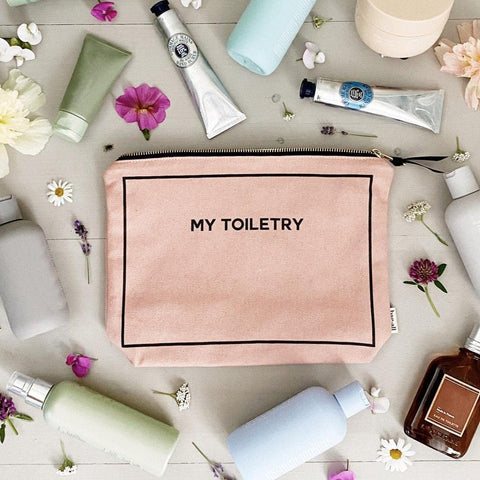 Bag-all Toiletry Travel Gift Set 4-Pack in pink blush cotton featuring My Toiletry pouch surrounded by beauty products and flowers on gray background, perfect for travel organization