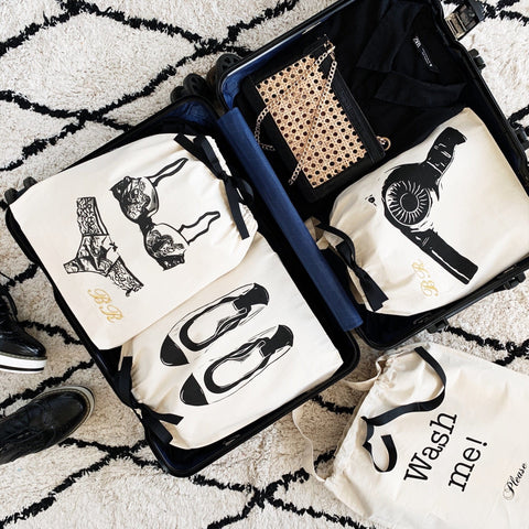 Bag-all Women's Travel Set 4-pack in cream features organized cotton bags for laundry, hairdryer, lingerie, and ballet flats, displayed neatly in an open suitcase on a black and white patterned rug