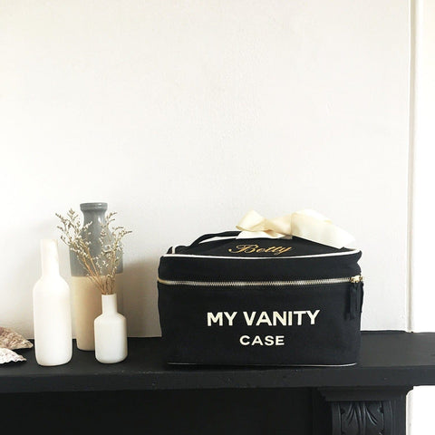 Bag-all My Vanity Large Beauty Box in classic black with elegant cream ribbon, displayed on dark shelf with decorative white vases and dried flowers