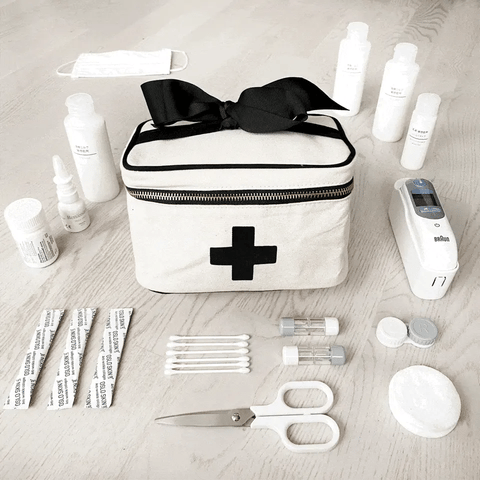 Bag-all Meds and First Aid Storage Box in cream with black cross print, black bow detail, zippered closure and carry handle, shown with medical supplies