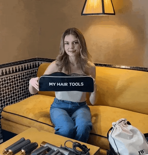 Bag-all Roomy Hair Wrap Tools Travel Case in black shown with styling tools on yellow couch, featuring heat-resistant lining and gold zipper, perfect for Dyson Airwrap storage