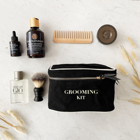 Bag-all Grooming Kit Box in black cotton with gold zipper, displayed with grooming essentials including wooden comb, shaving brush, and skincare products on marble surface