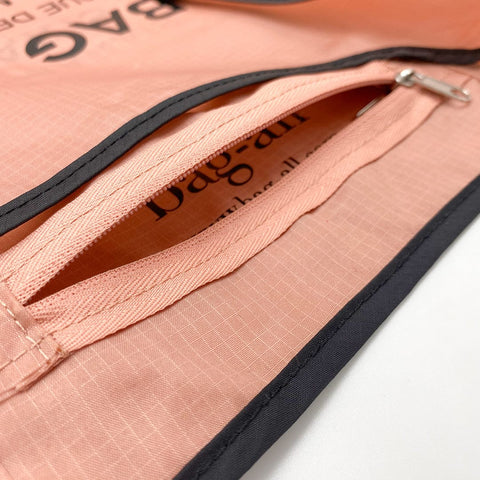 Bag-all Folding Shopping Bag with pink nylon material, featuring black trim and zipper pocket pouch detail. Close-up view showing durable reinforced stitching and textured fabric pattern.