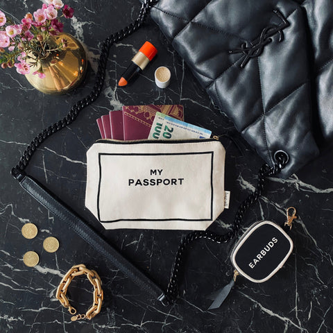 Bag-all Passport Pouch in cream cotton with passport, currency and travel essentials displayed on dark marble surface, showcasing practical travel organization and stylish design