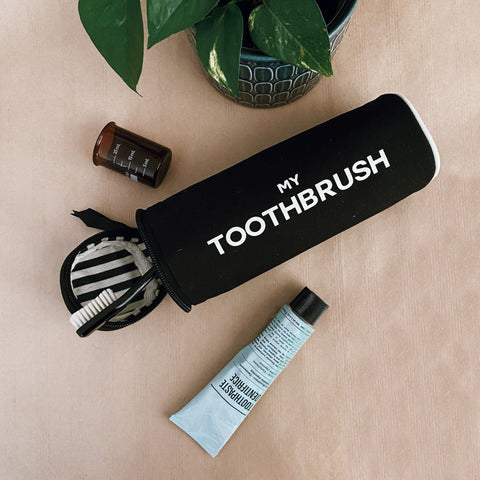 Black My Toothbrush case by Bag-all with toothbrush and toothpaste, part of the Toiletry Travel Gift Set Deal 4-Pack, shown with plant decor on beige surface