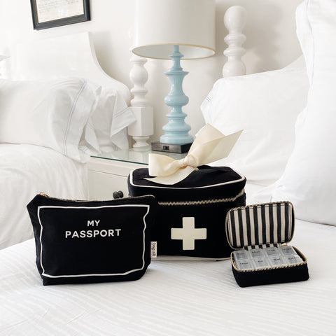 Bag-all First Aid Travel Gift Set 3-Pack in black cotton featuring passport pouch, first aid box, and pill case organizer on white bedding with blue lamp decor