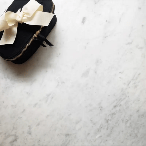 Bag-all black travel case with elegant cream bow and gold zipper detail on luxurious marble background