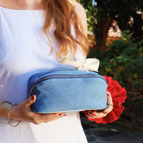 Woman holding a denim Accordion Box makeup and toiletry organizer by Bag-all with striped interior and elegant bow detail