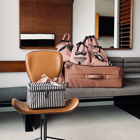 Bag-all Tennis Sneaker Shoe Bag in pink/blush displayed with striped makeup case on leather chair, showcasing organized travel accessories in modern home setting, perfect for stylish storage