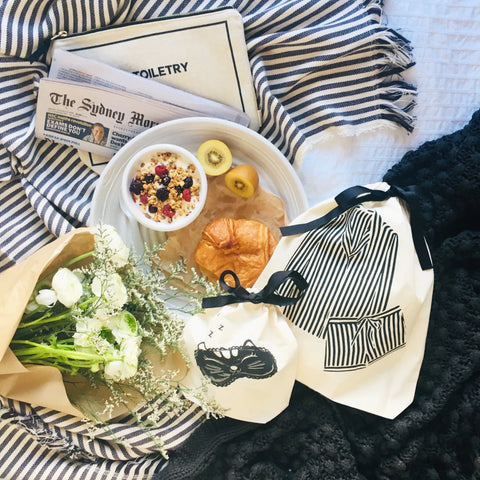 Bag-all Cat Sleepy Mask Bag in cream shown with breakfast setup, striped blanket, fresh flowers, newspaper and toiletries for perfect travel organization and relaxation essentials