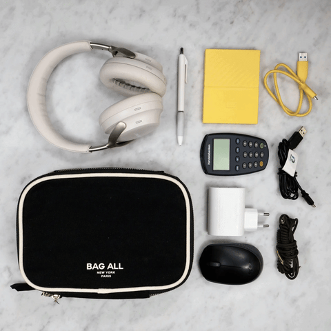 Black double-sided tech case with zipper, surrounded by headphones, cables, mouse, pen, calculator, and charger on marble surface