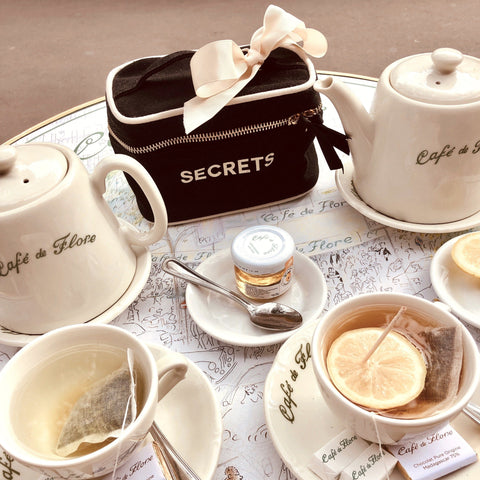 Bag-all Mini Beauty Box for Secrets in black with white bow, displayed among elegant tea settings with ceramic teapots and cups, showcasing its perfect size for storing small treasures