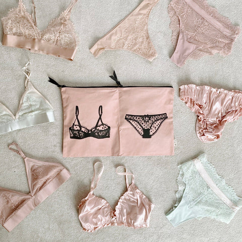 Bag-all Double Lingerie Packing Pouch in pink/blush features black lingerie illustrations, surrounded by delicate lace bras and panties in soft pink and white tones, perfect for organized travel storage