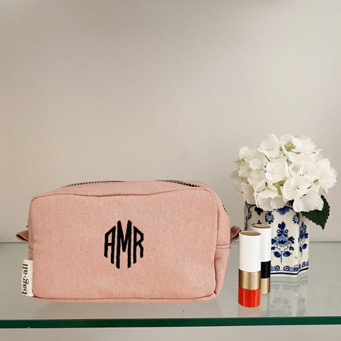 Bag-all personalized pink cotton cosmetic bag with black monogram initials, displayed next to white hydrangeas in blue and white vase and lipstick on glass surface