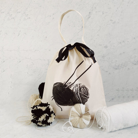 Bag-all Cream Knitting Bag with black yarn ball print, drawstring closure and handle, perfect for organizing knitting supplies and portable crafting projects