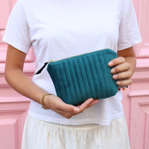 Woman holding a personalized quilted teal velvet makeup pouch with coated lining and gold zipper outdoors.