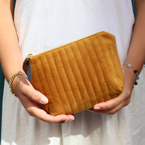 Hands holding a compact quilted yellow velvet makeup pouch with coated lining and zipper closure
