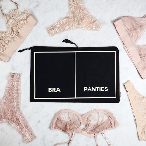 Black double underwear organizer pouch with labeled compartments for bras and panties on marble surface with lingerie.