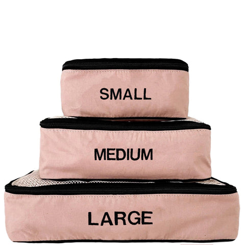 Stacked pink blush cotton packing cubes in small, medium, and large sizes with black zippers and monogrammed labels