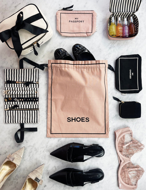 Bag-all Couture Shoe Travel Bag in blush pink with black text, shown with coordinating travel accessories, black and gold flats on marble surface