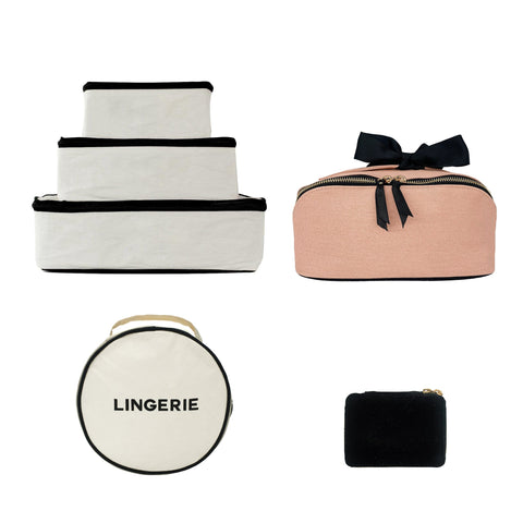 Bag-all Organized Traveler Essentials 4-set featuring stackable white storage cubes, pink cosmetic case with bow, round lingerie case, and black mini pouch for stylish travel organization