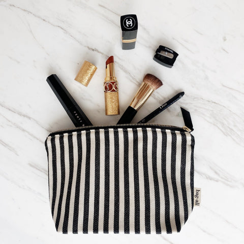 Bag-all Handbag Organizer Trio featuring striped makeup pouch with scattered cosmetics including gold lipstick, makeup brush, and beauty essentials on marble surface, showcasing practical organization and style