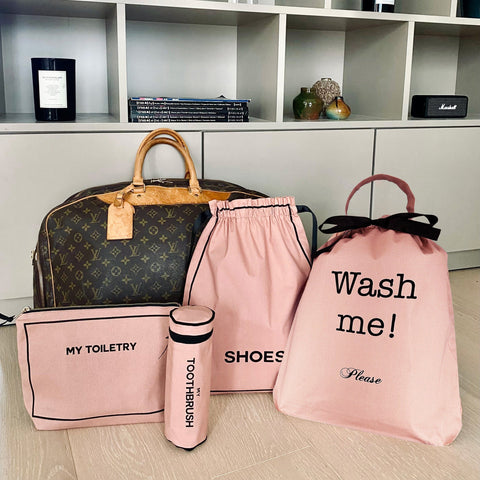 Bag-all Voyager Gift Set in Pink/Blush featuring toiletry pouch, toothbrush case, shoe bag, and wash me bag displayed with designer travel bag on white shelf storage