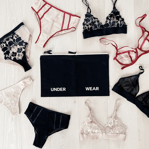 Bag-all Double Lingerie Packing Pouch in black with UNDER WEAR text, surrounded by matching lingerie sets in black, red, and beige, displayed on white wooden surface