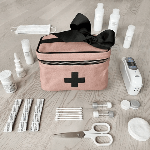 Bag-all Pink First Aid Storage Box with black cross design, stylishly displayed with medical supplies, cotton swabs, scissors and face mask. Features black bow and zipper closure.
