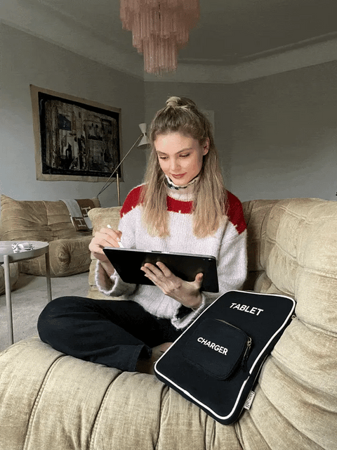 Bag-all 11" Black Tablet Case with charger pocket shown on couch, featuring padded protection and convenient storage compartment, perfect for protecting devices in style