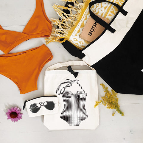 Bag-all Bretagne Swimsuit Travel Bag in cream cotton with vintage-style swimsuit print, recycled drawstring closure, displayed with orange bikini, sunglasses and beach accessories