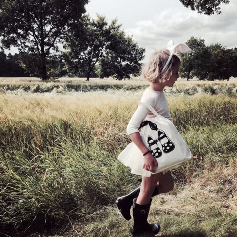 Bag-all Children Shoe Bag in cream cotton carrying shoes design, shown outdoors in natural wheat field setting, displaying practical storage solution for kids footwear